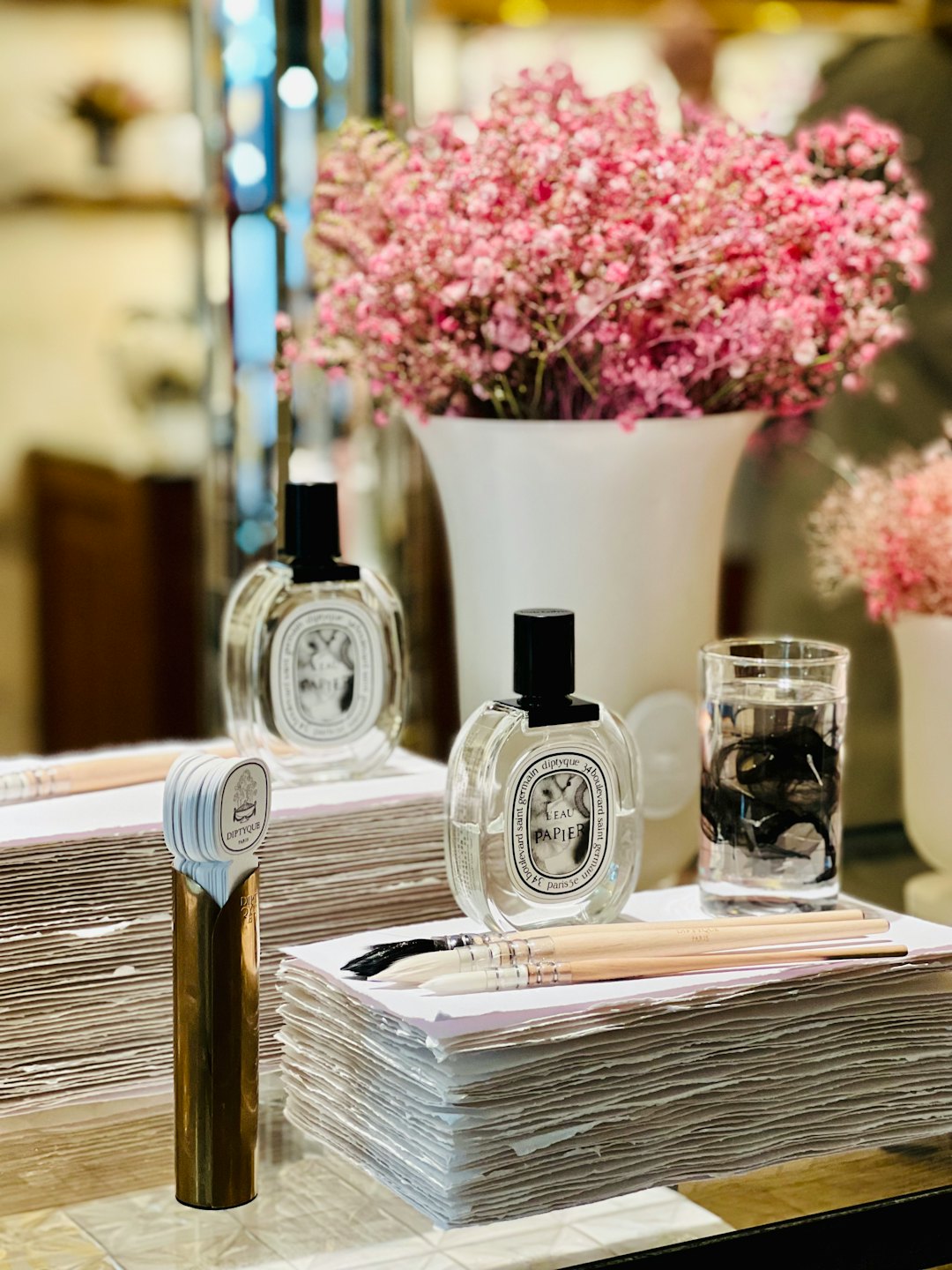 Diptyque perfume bottles with art supplies and flowers.